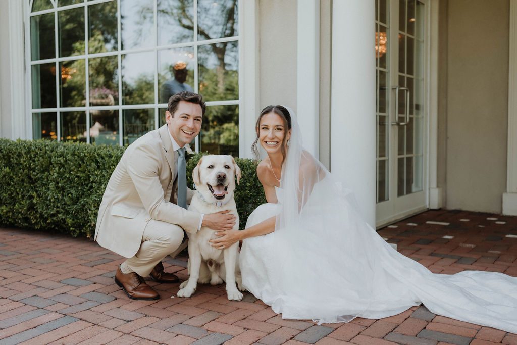 Bride and groom kneeling with their yellow lab on the patio