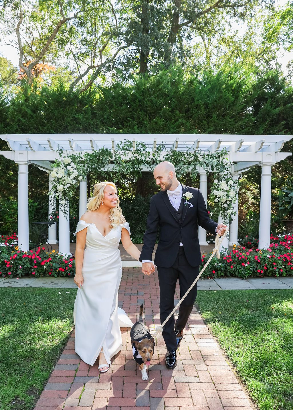 Newlyweds walk the brick aisle with their dog in a tuxedo